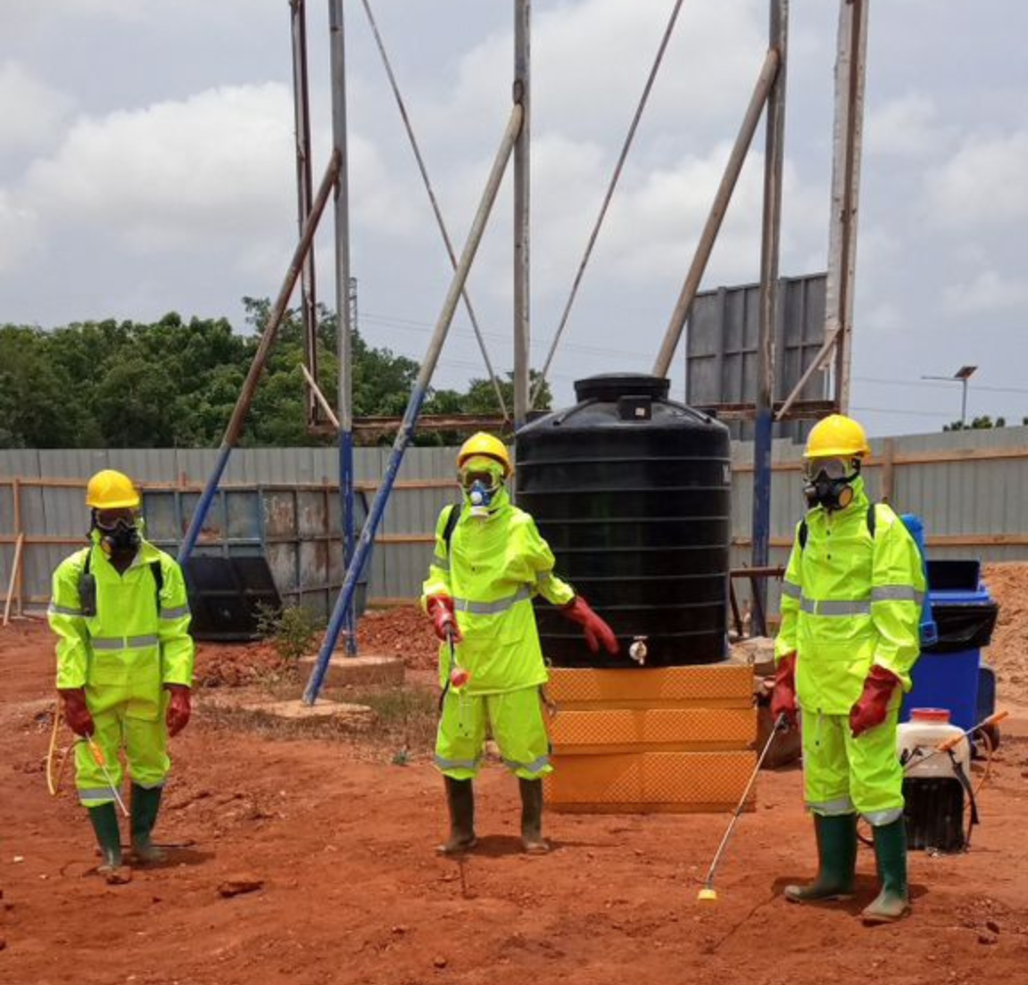 A group of men wearing protective gear whiles fumigating around a factory building